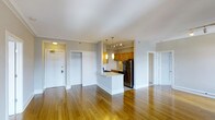 This single-floor residence offers a well-designed open-concept layout that maximizes both space and functionality. Warm hardwood flooring extends throughout, lending a cohesive and inviting character to the entire unit.

The living area is spacious and airy, benefiting from neutral white walls and smooth ceilings that amplify the sense of openness. Recessed and track lighting complement the ambient glow provided by pendant lights, ensuring the space is well-lit throughout the day.

At the heart of the home is a kitchen that opens directly onto the living area via a peninsula counter — ideal for casual dining or entertaining. The kitchen is equipped with honey-toned wood cabinetry, a stainless steel refrigerator, and a gas range, all framed by pendant lighting that adds a warm, focused glow to the workspace.

Multiple doorways lead to additional rooms, including what appears to be a closet or storage space near the entry, as well as access to further private rooms beyond. The front entry door is clearly defined, contributing to a practical and organized flow throughout the residence.

Overall, the space presents a clean, functional, and comfortable interior with a timeless aesthetic rooted in warm tones and thoughtful design.