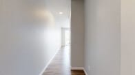 This one-bedroom, one-bathroom unit at 150 Main St in Longmont, Colorado offers a thoughtfully designed single-floor layout with modern finishes throughout. The open-concept living and kitchen area is anchored by warm wood-look plank flooring and a wall of vertical blinds that frame a sliding glass door, flooding the space with natural light and providing access to an outdoor view. The kitchen is well-appointed with two-tone cabinetry in light gray and dark wood, a classic white subway tile backsplash, stainless steel appliances including a refrigerator, range, microwave, and dishwasher, and recessed lighting overhead. The bedroom features a stylish sliding barn door as its entry, soft carpeted flooring, and clean neutral walls, lending a cozy yet contemporary feel. A secondary carpeted room offers flexible use as additional living space or a home office. The full bathroom is finished with large-format tile surrounding a soaking tub and shower combo, wood-toned cabinetry with a white quartz countertop, and coordinating wood-look flooring that ties the space together. Hallways connect each area efficiently, maximizing the functional use of the compact yet well-organized floor plan. The overall aesthetic is clean, modern, and move-in ready.