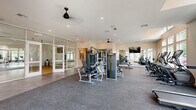 Located at 40 Pallet Rd in Candler, NC, this single-floor fitness center offers a generously sized, thoughtfully designed space for a comprehensive workout experience. The facility is divided into two primary areas: a main gym floor and a dedicated fitness studio.

The main gym floor is outfitted with rubber flooring and features an extensive selection of equipment, including multi-station cable machines, weight benches, treadmills, ellipticals, and stair climbers. A wall-mounted television and ceiling fans keep the environment comfortable and engaging. Large, multi-pane windows line the walls, allowing abundant natural light to fill the space and offering views of the surrounding outdoor scenery. Soaring ceilings add to the open, airy atmosphere.

The adjoining fitness studio is separated from the main floor by sleek floor-to-ceiling glass partition walls with double doors, providing visual connectivity while maintaining a distinct space. The studio features smooth hardwood-style flooring, full-length wall mirrors, and a rack of medicine balls and dumbbells, making it well-suited for yoga, stretching, group fitness, or functional training. Ceiling fans and ample natural light from surrounding windows complete the inviting environment. Together, the two areas form a versatile, modern fitness facility.