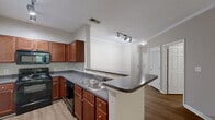 This single-floor residence at 940 Timber Valley Way in Virginia Beach, Virginia, offers a thoughtfully designed layout with a neutral color palette and a blend of hard and soft flooring surfaces throughout. The kitchen serves as a functional centerpiece, featuring rich cherry-toned cabinetry, dark granite-style countertops, and a suite of black appliances including a refrigerator, range, microwave, and dishwasher. A peninsula with an overhang provides additional workspace and casual seating, while track lighting overhead adds a modern touch. Crown molding carries through into the living area, which is finished with plush carpeting and a ceiling fan, lending a comfortable, polished feel. Bedrooms are carpeted and generously proportioned, with neutral walls and ample closet space, including at least one walk-in closet with wire shelving. Select rooms benefit from natural light through window treatments, and one room opens directly onto an outdoor deck with views of surrounding greenery. Two full bathrooms are present, each featuring a tub-shower combination with white tile surrounds and chrome fixtures, with one bathroom showcasing wood-look flooring for a clean, updated aesthetic.