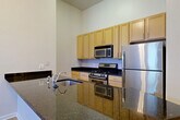 Located at 1200 N Herndon St in Arlington, VA, this two-bedroom, one-bathroom residence offers a thoughtfully designed single-level layout with generous living space. Soaring ceilings throughout create an open, airy atmosphere, while light-toned hardwood-style flooring flows seamlessly from room to room.

The kitchen is a standout feature, equipped with stainless steel appliances including a gas range, microwave, and refrigerator. Rich dark granite countertops complement the warm wood cabinetry, and a peninsula with additional counter space connects the kitchen to the combined dining and living area, making it ideal for both everyday living and entertaining.

The living and dining area benefits from large windows and a glass-paneled entry door that floods the space with natural light. The generously sized primary bedroom features tall ceilings and multiple windows, while the second bedroom mirrors this bright, open feel. Both rooms offer ample closet space — the unit includes five closets in total.

The bathroom is clean and bright, featuring white tile walls, a soaking tub, and mosaic tile flooring. Additional conveniences include a dedicated laundry area and two entrance points. The overall ambiance is modern, clean, and well-lit, presenting a comfortable and functional living environment in the heart of Arlington.