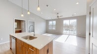 This contemporary single-floor residence offers a thoughtfully designed open-concept layout that seamlessly connects the kitchen, dining, and living areas. The kitchen serves as the centerpiece, featuring a large island with a quartz countertop, an undermount stainless steel sink with a professional-style faucet, warm wood-toned cabinetry paired with high-gloss white upper cabinets, and a full suite of stainless steel appliances. Elegant pendant lighting above the island adds a refined touch, while recessed lighting and soaring ceilings enhance the sense of volume throughout. Light-toned wood plank flooring flows through the main living areas, complementing the neutral gray palette of the walls. The spacious living area is bathed in natural light from large windows and a glass sliding door that opens to a private balcony, offering outdoor views. A ceiling fan overhead adds both comfort and style. The bedrooms are carpeted for warmth and comfort, each benefiting from abundant natural light and ample closet space with built-in shelving. The bathroom is well-appointed with a soaking tub and shower combination, a wood-toned vanity with quartz countertop, and a backlit mirror that adds a modern, functional accent. The overall ambiance is clean, bright, and contemporary throughout.