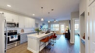 This thoughtfully designed one-bedroom, one-bathroom unit in Charlotte, NC offers an efficient yet stylish layout across a single floor. The open-concept kitchen and living area serves as the heart of the space, with the kitchen showcasing two-tone cabinetry—white upper cabinets paired with soft gray-blue lower cabinets—complemented by quartz countertops, a subway tile backsplash, stainless steel appliances, and a central island with seating. Recessed lighting and pendant fixtures illuminate the space, while hardwood-style flooring flows throughout.

The living room receives ample natural light through large windows and a glass door, with a ceiling fan adding comfort. The bedroom features a striking dark accent wall with gold detailing, two windows overlooking the outdoors, a ceiling fan, and direct access to a dedicated walk-in closet outfitted with wire shelving on multiple levels.

The bathroom is well-appointed with gray-blue vanity cabinetry, a white quartz countertop, a tub-shower combination, wood-look flooring, and a wall-mounted shelving unit for storage. The unit's neutral color palette, modern fixtures, and cohesive design elements create a clean, contemporary ambiance throughout.
