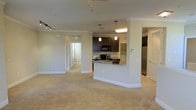 This single-floor residence offers an open and airy layout that seamlessly connects the living, dining, and kitchen areas. The space is finished with plush wall-to-wall carpeting and crisp white crown molding, lending a clean and polished aesthetic throughout.

The kitchen serves as a central focal point, featuring rich dark cabinetry that contrasts elegantly with granite countertops. A peninsula with an integrated sink provides a convenient breakfast bar and additional prep space, while pendant lighting above adds a warm, stylish glow. Stainless steel appliances, including a full-size refrigerator and built-in microwave, complete the well-appointed culinary space.

Track lighting in the living area offers flexible illumination across the open floor plan, which flows naturally into adjacent rooms visible through open doorways. The neutral color palette of warm beige tones throughout the walls and flooring creates a welcoming and versatile canvas, suitable for a variety of furnishing styles.

The layout is thoughtfully designed to maximize the sense of space and connectivity between rooms, making it ideal for both everyday living and entertaining. The overall ambiance is modern yet approachable, with quality finishes and practical features that enhance the day-to-day living experience.