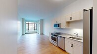 Located at 161 S Huntington Ave in Boston's Jamaica Plain neighborhood, this well-designed one-bedroom, one-bathroom residence offers a thoughtful layout across a single floor. The open-plan kitchen and living area serves as the heart of the home, featuring light hardwood flooring that enhances the bright, airy feel of the space. The kitchen is outfitted with stainless steel appliances — including a range, dishwasher, microwave, and refrigerator — complemented by crisp white shaker cabinetry and granite countertops. Floor-to-ceiling windows along the living area face the street, flooding the space with natural light and offering views of the surrounding neighborhood. The bedroom provides a comfortable retreat with plush carpeting, a large window with outdoor views, and access to a spacious walk-in closet equipped with built-in shelving and additional carpet flooring. The full bathroom features clean tile flooring, a modern vanity, and a well-lit mirror. Neutral tones and clean lines throughout the residence create a contemporary and functional living environment well-suited for urban Boston living.