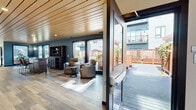 Located at 1001 Belknap St in Superior, Wisconsin, this thoughtfully designed single-floor amenity space offers a generous footprint that blends contemporary interior finishes with seamless outdoor connectivity. The interior is defined by striking wood-slat ceilings that run throughout, adding warmth and architectural character to the space. Wide-plank hardwood-style flooring complements the deep teal accent walls, creating a modern yet inviting atmosphere.

The layout includes a comfortable lounge area furnished with reclining leather chairs and a side table, bathed in natural light streaming through large floor-to-ceiling windows. A casual dining and social zone features high-top bar tables and industrial-style stools, ideal for gathering. A bar counter with seating provides an additional focal point, while a hallway corridor leads to private rooms or utility spaces, keeping the layout organized and functional.

Large glass doors open directly onto an expansive outdoor deck constructed with rich hardwood materials, featuring built-in bench seating, privacy panels, and landscaped greenery. The exterior facade is clad in warm cedar-toned siding, lending a refined and cohesive appearance to the structure. The outdoor area includes paved pathways, raised planter beds, and open gathering zones, making it well-suited for year-round use in a multi-residential community setting.