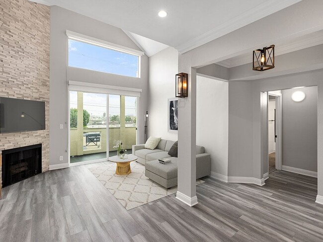 Hardwood floored living room with view of stone accent wall, fireplace, and high third-floor ceilings. - Palms Court