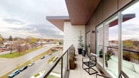 This contemporary single-floor residence showcases a refined modern design defined by clean lines, a neutral palette, and high-quality finishes throughout. The interior is anchored by large-format light-toned tile flooring that runs seamlessly from the entryway through the hallways, contributing to a cohesive and polished aesthetic. A bright, airy entry corridor features floor-to-ceiling glazing framed in sleek black metal, allowing natural light to pour into the space while offering a view to the outdoor surroundings.

A generously proportioned hallway connects the main areas of the residence, its white walls and recessed lighting creating an open, gallery-like atmosphere. Curated wall art adds a touch of personality along the passage. The space also benefits from smart home integration elements visible along the corridor walls.

The private balcony is a standout feature, clad in warm wood-paneled ceilings and finished with large cream-toned floor tiles. Framed by a sleek glass-and-metal railing, the balcony offers sweeping elevated views of the surrounding urban landscape, including tree-lined streets and the wider neighborhood. Tasteful potted greenery enhances the outdoor area, making it an inviting retreat. The exterior facade combines cream-toned masonry with dark metal accents, reflecting the building's contemporary architectural character.