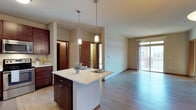This single-floor residence offers a thoughtfully designed open-concept layout that seamlessly connects the kitchen, dining, and living areas. The kitchen is a standout feature, showcasing rich dark-wood cabinetry, light-toned countertops, and a full suite of stainless steel appliances including a range, over-the-range microwave, dishwasher, and refrigerator. A central island with pendant lighting above serves as both a prep space and casual dining area, adding both function and visual appeal. Light wood-style flooring runs throughout the main living areas, complementing the warm, neutral color palette of the walls and trim.

The living area is generously proportioned with access to a private balcony through a sliding glass door, allowing for abundant natural light and outdoor views. A pendant light fixture anchors the dining space, which flows naturally from the kitchen island.

The bedrooms are carpeted for comfort, with neutral walls and wood trim detailing. Each room benefits from natural light through well-placed windows, and closet access is provided. The bathroom features rich dark-wood vanity cabinetry, a granite-style countertop, a wide mirror with overhead lighting, and a tub-shower combination. Overall, the space presents a cohesive and comfortable living environment with quality finishes throughout.