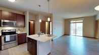 This single-floor residence offers a thoughtfully designed open-concept layout that seamlessly connects the kitchen, dining, and living areas. The kitchen is a standout feature, showcasing rich dark-wood cabinetry, light-toned countertops, and a full suite of stainless steel appliances including a range, over-the-range microwave, dishwasher, and refrigerator. A central island with pendant lighting above serves as both a prep space and casual dining area, adding both function and visual appeal. Light wood-style flooring runs throughout the main living areas, complementing the warm, neutral color palette of the walls and trim.

The living area is generously proportioned with access to a private balcony through a sliding glass door, allowing for abundant natural light and outdoor views. A pendant light fixture anchors the dining space, which flows naturally from the kitchen island.

The bedrooms are carpeted for comfort, with neutral walls and wood trim detailing. Each room benefits from natural light through well-placed windows, and closet access is provided. The bathroom features rich dark-wood vanity cabinetry, a granite-style countertop, a wide mirror with overhead lighting, and a tub-shower combination. Overall, the space presents a cohesive and comfortable living environment with quality finishes throughout.