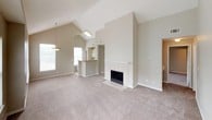 This single-floor residence offers a well-organized layout with a variety of functional spaces throughout. The living room serves as the central gathering area, highlighted by dramatic vaulted ceilings, soft neutral-toned carpet, and a tile-surround fireplace that anchors the room. Natural light flows in through multiple windows, and a breakfast bar connects the living area to the kitchen, creating an open, airy feel. A pendant light fixture accents the transition between spaces.

The kitchen is equipped with cream-toned cabinetry, laminate countertops, a stainless steel sink, and white appliances including an electric range and built-in microwave. An open shelving nook adjacent to the kitchen provides additional storage.

The bedrooms are generously sized, each featuring soft carpeting, ceiling fans with light fixtures, and ample natural light. The primary bedroom includes a walk-in closet with built-in shelving, while additional bedrooms offer standard closet storage and windows with blinds.

Two full bathrooms include soaking tub and shower combinations, light wood cabinetry, and tile flooring, providing practical and comfortable facilities. A dedicated laundry area houses a full-size washer and dryer alongside a water heater, completing the home's self-contained utility needs.