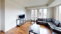 This well-designed multi-bedroom unit spans a single floor and offers a cohesive blend of modern finishes and functional living spaces. The living room is anchored by large windows that frame urban views and flood the space with natural light, complemented by warm hardwood flooring throughout. A dedicated media area provides ample room for seating and entertainment.

The kitchen is a standout feature, equipped with rich dark-wood cabinetry, granite countertops, stainless steel appliances including a range, microwave, and refrigerator, and a peninsula with a double sink. Track and pendant lighting enhance both functionality and ambiance. A sliding glass door opens to a private balcony with open city views.

The bedrooms are generously sized, each with hardwood floors, large windows, and ample natural light. The unit includes two bathrooms: a full bath with a double-sink granite vanity, dark cabinetry, and a tub-shower combo, and a second bath featuring a single granite-top vanity and a walk-in shower. Tile flooring is consistent throughout both bathrooms, maintaining a clean, polished aesthetic across the entire unit.