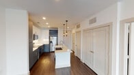 Located at 201 S Calhoun St in Fort Worth, Texas, this single-floor residence offers a thoughtfully designed layout with contemporary finishes throughout. Dark hardwood-style flooring flows through the main living and kitchen areas, providing a warm contrast against the crisp white walls and ceilings outfitted with recessed lighting.

The kitchen serves as a focal point of the space, featuring a central island with an undermount sink and pendant lighting overhead. Two-tone cabinetry pairs white upper cabinets with slate-blue lower units, complemented by a classic subway tile backsplash and stainless steel appliances, including a French door refrigerator, range, and over-the-range microwave. A built-in wine rack adds a distinctive design element above the refrigerator.

The open living area provides a generous, versatile space with clean lines and recessed lighting. A separate room with French doors offers abundant natural light and outdoor views, while a carpeted bedroom includes a ceiling fan and a window with exterior views. The bathroom is well-appointed with tile flooring, a vanity with a white countertop, dark cabinetry, a glass-enclosed shower with subway tile surround, and direct access to a spacious walk-in closet with built-in shelving.