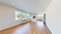 Located at 35 Spring St in Wallington, NJ, this thoughtfully laid-out single-floor unit offers a clean, modern aesthetic throughout. Warm hardwood flooring flows seamlessly across the main living areas, complementing the crisp white walls and recessed lighting that give the space a bright, airy feel.

The open-concept living and dining area is generously proportioned, with large windows on multiple sides that flood the room with natural light and provide pleasant views of the surrounding tree-lined neighborhood. A wall-mounted HVAC unit ensures year-round comfort.

The kitchen is a standout feature, boasting tall white shaker-style cabinetry that extends to the ceiling for ample storage, a white peninsula with a sink, and a full suite of stainless steel appliances including a gas range, microwave, dishwasher, and refrigerator. The layout allows for easy interaction between the kitchen and living areas.

The bathroom is finished in a clean, contemporary style with light tile flooring, a white vanity, and bright white walls. In-unit laundry adds everyday convenience. The entrance hall leads efficiently to each area of the unit, and three closets — including what appears to be a walk-in — provide excellent storage capacity throughout.