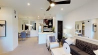 This single-floor residence showcases a thoughtfully designed open-concept layout that seamlessly connects the living, dining, and kitchen areas into one cohesive, light-filled space. The interior is finished in a contemporary palette of crisp whites and deep espresso tones, creating a clean and sophisticated ambiance throughout.

The kitchen is outfitted with dark cabinetry, stainless steel appliances, and a central peninsula with a white waterfall countertop that doubles as a casual breakfast bar. Industrial-style pendant lights hang above the peninsula, adding a refined accent to the space. Recessed lighting and a modern ceiling fan with a sleek dark finish keep the main living area bright and comfortable.

The living area offers generous proportions, with plush neutral carpeting underfoot and ample room for stylish furnishings. A separate dining nook, visible through a mirrored wall, adds depth and dimension to the overall layout.

A private balcony with contemporary metal railings extends the living space outdoors, offering views of a resort-style pool area flanked by mature palm trees and desert landscaping — an inviting outdoor retreat ideal for enjoying the sunny surroundings.