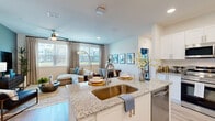 This single-floor residence offers a well-organized layout across two bedrooms, one bathroom, and a dedicated laundry room, with two closets providing ample storage throughout. The open-concept kitchen and living area form the heart of the home, with the kitchen showcasing white shaker cabinetry, granite countertops, stainless steel appliances, and a central island with a deep single-basin sink. Light wood-style flooring runs throughout, complementing the neutral, modern aesthetic. The living room receives generous natural light through large windows with exterior views, and features a ceiling fan overhead.

The primary bedroom includes a ceiling fan, a window with an outdoor view, and a bold teal accent wall that adds a distinctive design element. The bathroom is finished with a granite-topped white vanity, wood-style flooring, a tub-shower combination with tile surround, and recessed lighting. A dedicated laundry room houses a full-size side-by-side washer and dryer. Recessed lighting throughout and a cohesive neutral color palette contribute to the home's clean, contemporary ambiance.
