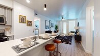 This single-floor residence offers a thoughtfully designed open-concept layout that seamlessly connects the kitchen, dining, and living areas. The kitchen is equipped with stainless steel appliances, including a refrigerator, range, and over-the-range microwave, complemented by gray shaker-style cabinetry, white quartz countertops, and a classic subway tile backsplash. A central island with an integrated sink and bar seating serves as both a functional workspace and a casual dining spot, with pendant lighting adding a modern touch overhead.

The living area is bright and inviting, featuring wood-look flooring, a ceiling fan, and a glass door that fills the space with natural light. Two bedrooms offer carpeted floors, ample natural light through large windows, and comfortable proportions for furnishing. The primary bedroom includes notable storage with a mid-century-inspired wardrobe, while both rooms maintain a calm, neutral aesthetic.

Two full bathrooms mirror the home's clean design language, each featuring gray vanity cabinetry, white quartz countertops, wood-look flooring, and a tub-shower combination. Throughout the residence, white walls and consistent finishes create a cohesive, modern ambiance suitable for a variety of lifestyles.