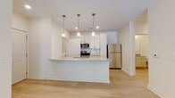 Located at 659 Treeland Dr in Ladson, South Carolina, this single-story home presents a clean, contemporary design throughout its open-concept floor plan. The interior is finished with light, neutral tones and modern materials that create a bright, cohesive atmosphere from room to room.

The kitchen serves as the centerpiece of the main living area, anchored by a substantial island topped with speckled granite countertops and an integrated sink. White shaker-style cabinetry extends to the ceiling, complemented by a subway tile backsplash and a full suite of stainless steel appliances, including a refrigerator, range, and built-in microwave. Three pendant lights hang above the island, adding focused illumination and a polished aesthetic detail.

Light wood-style flooring flows through the open kitchen and living areas, while the bedrooms feature plush carpeting underfoot. Each bedroom benefits from large windows fitted with blinds, allowing generous natural light and outdoor views, and ceiling fans provide additional comfort. A spacious walk-in closet with wire shelving offers practical storage.

The bathroom features a granite-topped vanity with light wood cabinetry and a well-lit mirror, maintaining the home's consistent, modern finish. A door off the living area provides direct outdoor access, further enhancing the airy, connected feel of this well-appointed home.