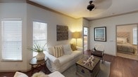 This single-floor residence offers a thoughtfully designed layout that balances comfort and functionality across its living spaces. The kitchen serves as a central highlight, featuring rich dark cabinetry that extends to the ceiling, granite-style countertops, a peninsula with seating, stainless steel appliances including a refrigerator, range, and microwave, and track lighting overhead. Hardwood flooring and crown molding lend a refined character to this space, which opens toward the dining and living areas.

The dining area accommodates a round table surrounded by upholstered chairs, with natural light filtering through blinds and framed artwork adorning the walls. The living room is warm and inviting, centered around a white sofa, a vintage-style trunk coffee table, and a ceiling fan overhead. Multiple windows allow generous natural light throughout.

The primary bedroom features plush carpeting, a ceiling fan, multiple windows, and direct access to a walk-in closet with built-in shelving. A second bedroom also offers carpet flooring, natural light, and dedicated desk space. The bathroom presents dual sinks set in dark cabinetry with granite-style counters, a large framed mirror, hardwood flooring, and a full tub-shower combination, completing this well-finished residence.
