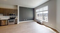 Located at 1455 W Lake St in Minneapolis, Minnesota, this single-floor unit offers a thoughtfully designed layout with modern finishes and a clean, contemporary aesthetic. The kitchen is a standout feature, equipped with full-height dark wood-grain cabinetry, light quartz countertops, a classic white subway tile backsplash, and a complete suite of stainless steel appliances including a refrigerator, range, over-the-range microwave, and dishwasher. Light hardwood-style flooring runs throughout the main living areas, complementing the neutral gray wall palette and creating a cohesive, modern feel. The open living area benefits from a large window that invites generous natural light and provides views of the surrounding neighborhood. A bold charcoal accent wall adds depth and visual interest to the living space. The bedroom area includes a closet and recessed lighting, maintaining the unit's clean lines. The bathroom features a wood-framed mirror, warm wood vanity cabinetry, a soaking tub, and white subway tile surround, offering a calm and functional retreat. Overall, the space presents a well-balanced combination of modern design and practical living.