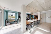Located at 526 Hartford Tpke in Shrewsbury, MA, this single-floor communal amenity space offers a well-appointed and thoughtfully designed environment spanning just over 1,000 square feet. The layout flows seamlessly between two distinct functional zones, each with its own character and purpose.

The lounge area anchors one end of the space, featuring a teal-accented fireplace wall clad in diamond-patterned tile, flanked by open built-in shelving. Comfortable sectional seating, curated artwork, and decorative accents create a warm, inviting atmosphere. Large glass doors flood the area with natural light and provide views of the outdoor terrace, enhancing the sense of openness.

Transitioning through the space, a dedicated dining zone features a long communal table with mixed seating, suspended over an eye-catching geometric-patterned tile floor. A stylish multi-lamp chandelier anchors the table from above, adding a refined touch.

Adjacent to the dining area, a fully equipped kitchenette serves as a functional hub, outfitted with dark cabinetry, white quartz countertops, a stainless steel sink, a beverage refrigerator, and a dedicated coffee bar station. A large picture window above the sink offers views of the surrounding landscape, bringing in abundant natural light. The coffered ceiling detail, teal accent walls, and light-toned tile flooring unify the entire space with a cohesive, contemporary aesthetic.