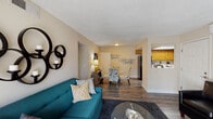 Located in the Woodland Hills neighborhood of Colorado Springs, Colorado, this single-floor residence offers a well-organized layout connecting living, dining, and kitchen spaces in a cohesive flow. The living room is a comfortable focal point, featuring a tiled fireplace, a wall-mounted television, and a sliding glass door that opens to an outdoor view, allowing natural light to fill the space. Durable wood-style flooring runs throughout the main living and dining areas, adding warmth and continuity. The dining area sits adjacent to the living room and connects directly to the kitchen, making it well-suited for entertaining. The kitchen is equipped with warm oak cabinetry, black appliances including a refrigerator, range, microwave, and dishwasher, white countertops, and a notable skylight that brightens the workspace. Both bedrooms feature plush carpeting and windows with outdoor views. The primary bedroom is generously proportioned with room for substantial furniture. The two bathrooms include wood-style flooring, a tub-shower combination, built-in shelving for storage, and a sliding mirrored closet door. Throughout the residence, a textured ceiling, neutral wall tones, and clean white trim establish a consistent and understated aesthetic.
