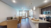 This single-floor residence offers a thoughtfully designed open-concept layout that seamlessly connects the kitchen, dining, and living areas. The kitchen is a standout feature, showcasing rich dark cabinetry, granite countertops, a large center island with a built-in sink, stainless steel appliances, and elegant pendant lighting overhead. Hardwood-style flooring runs throughout the main living spaces, complementing the neutral, warm color palette.

The living area is bright and welcoming, benefiting from multiple windows that invite generous natural light and offer outdoor views. A ceiling fan adds to the comfort of the space. The dining area flows naturally from both the kitchen and living room, creating an ideal setting for entertaining.

The bedrooms are carpeted for comfort, each featuring ceiling fans and windows with ample natural light. One bedroom includes a private en-suite bathroom with a tiled soaking tub, granite vanity countertop, and access to a generously sized walk-in closet outfitted with built-in shelving and dual hanging rods on either side — providing exceptional storage capacity.

Crown molding and recessed lighting add refined architectural detail throughout, while the cohesive neutral tones create a calm, inviting ambiance across the entire residence.
