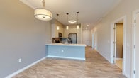 This single-floor residence showcases a thoughtfully designed open-concept layout that seamlessly connects the kitchen and living areas. The kitchen is a standout feature, equipped with cream shaker-style cabinetry, stainless steel appliances including a French door refrigerator, electric range, and built-in microwave. A mosaic tile backsplash adds visual interest, while a peninsula with a white countertop and integrated sink provides additional workspace and casual seating. Pendant lighting and recessed fixtures illuminate the space, which flows over light wood-look flooring throughout the main areas.

The bedrooms are carpeted in a neutral gray tone, offering a comfortable feel underfoot. Each room benefits from natural light through blinded windows, and ceiling fans provide added comfort. The two bathrooms are finished with large-format tile flooring and cream vanities with white countertops. One bathroom features a tiled soaking tub, while the other includes a glass-enclosed shower with a decorative mosaic tile accent. A dedicated laundry room houses a full-size washer and dryer with overhead shelving. Crown molding and consistent neutral walls tie the entire space together cohesively.