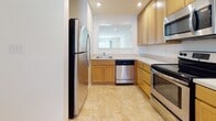 Located at West Creek Village Apartments in Elkton, Maryland, this single-floor residence is designed with functionality and comfort in mind. The kitchen is a standout feature, outfitted with warm-toned wood cabinetry, light-colored countertops, and a full suite of stainless steel appliances including a refrigerator, dishwasher, electric range, and over-the-range microwave. A pass-through window connects the kitchen to the adjacent living area, enhancing the open feel of the space. Recessed lighting illuminates the kitchen's tile flooring, which flows seamlessly throughout the main living and dining areas. The living room is generously sized, featuring plush wall-to-wall carpeting and access to other areas of the home via a paneled door. Bedroom areas continue the carpeted flooring and are filled with natural light from large windows that offer views of the surrounding greenery. The bathroom is clean and functional, featuring tile flooring, a full-sized soaking tub with shower, and a wood-vanity with countertop. A dedicated laundry room with a full-sized washer and dryer provides added everyday convenience. The overall ambiance is bright, clean, and practical throughout.