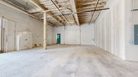 Located at 127 N Elizabeth St in Lima, Ohio, this single-floor commercial space offers a compelling mix of industrial character and refined architectural detailing. The layout is defined by expansive open areas with polished concrete floors throughout, providing a durable and versatile foundation suited to a wide range of uses. A standout central corridor features elegant crown molding, warm wood-paneled accents, and bold steel-framed glass partitions that divide the space while maintaining visual openness and an abundance of natural light. Modern circular pendant fixtures and wall sconces illuminate the corridor with a polished, contemporary feel. Street-facing entries include full-lite glass double doors that invite natural light deep into the interior. Adjacent open areas feature soaring exposed truss ceilings with visible structural framing, white-painted masonry walls, and concrete support columns, creating a raw, loft-like atmosphere with significant volume. A glass-railed stairwell adds a sleek architectural element connecting areas at varying levels. The steel-framed glass wall system seamlessly unites the refined corridor with the more industrial open zones, offering a dynamic spatial contrast. This adaptable space presents strong potential for retail, creative office, showroom, or mixed-use commercial occupancy.