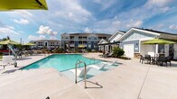 Located at 3963 Woolcock Dr in Myrtle Beach, South Carolina, this single-story amenity space serves as a central gathering hub within a well-appointed residential community. The exterior architecture combines classic coastal design with refined material choices, most notably the striking stacked stone accent walls that incorporate rich tones of rust, tan, and charcoal. These stone elements are paired with blue-gray horizontal lap siding and crisp white trim, creating a visually cohesive and polished aesthetic.

The centerpiece of the outdoor environment is a generously sized swimming pool with clear, turquoise water, accessible via sleek entry steps and handrails. The expansive concrete pool deck is outfitted with modern chaise lounges and wicker seating with neutral cushions, providing ample space for relaxation under the open South Carolina sky.

Adjacent to the pool, a covered patio offers a shaded lounge area furnished with comfortable wicker seating arrangements, ideal for socializing or unwinding. Stacked stone columns anchor the covered structure, reinforcing the architectural character seen throughout the space. White-paned glass doors with grid detailing provide entry points and allow natural light to filter through. Lush landscaping and manicured greenery frame the perimeter, enhancing the overall resort-like ambiance of this outdoor amenity space.