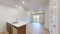 This efficient one-bedroom, one-bathroom unit is thoughtfully laid out to maximize functionality and comfort. The open-concept kitchen and living room area serves as the heart of the space, featuring light wood-look flooring that runs throughout. The kitchen is equipped with stainless steel appliances — including a refrigerator, range, and microwave — complemented by rich, dark wood cabinetry and a striking marble-look countertop peninsula with an integrated double sink. Recessed lighting illuminates the space overhead, enhancing the clean, contemporary aesthetic.

The living area benefits from soaring vaulted ceilings and direct access to a private balcony through sliding glass doors, allowing for an abundance of natural light and outdoor views. An additional window in the adjacent bedroom further brightens the unit, which also includes a wall-mounted HVAC unit for individualized climate control.

The bedroom is a cozy yet well-proportioned retreat, while a dedicated closet provides practical storage. The bathroom features a full tub-shower combo with a curved curtain rod, neutral toned walls, and a marble-look vanity surface that ties in cohesively with the kitchen finishes. Throughout the unit, the neutral color palette and modern touches create a clean, inviting atmosphere.