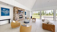 Located at 102 Lusk Lane in Pooler, Georgia, this poolside game room is a thoughtfully designed recreational space that seamlessly blends indoor comfort with outdoor connectivity. The single-floor layout is anchored by dramatic vaulted ceilings clad in white beadboard, which amplify the sense of openness and airiness throughout the space. Large ceiling fans complement the architectural height, ensuring comfortable airflow year-round.

Floor-to-ceiling screened windows and black-framed glass panels wrap around the perimeter, flooding the interior with abundant natural light and offering unobstructed views of the surrounding pool area and lush Georgia landscape. The polished concrete terrazzo flooring adds a clean, durable foundation that ties the modern coastal aesthetic together.

The main gathering area features a striking full-height brick fireplace wall with a built-in television, serving as the room's focal point. Wicker lounge chairs and soft seating are arranged to encourage relaxed conversation around the fireplace, while coastal-inspired artwork adds character to the white shiplap walls. A central shuffleboard table provides a dedicated entertainment zone, complemented by additional lounge seating along the screened perimeter. Multiple access points connect directly to the outdoor pool deck, making this space an ideal hub for social gatherings and recreation.