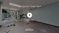 The gym at 4700 Westgrove Street in Raleigh, North Carolina, is a single-floor fitness facility designed to accommodate a range of workout needs. The space features a practical, open layout with distinct zones for cardio training, strength work, and functional exercise. Walls painted in a calming light blue set a clean, motivating tone throughout, while large floor-to-ceiling mirrors along one side visually expand the space and allow users to monitor their form during workouts.

The cardio area is equipped with a stationary recumbent bike and treadmills, positioned to take advantage of natural light from windows offering outdoor views. A stability ball and exercise mat provide a dedicated space for stretching and functional training. The strength training zone features a multi-station cable and weight machine, a weight bench, and an assortment of dumbbells, catering to both beginner and experienced lifters.

Flooring transitions between carpeted and hard rubber-tiled surfaces, strategically zoning the space for different activity types. The drop ceiling with recessed panel lighting ensures consistent, even illumination throughout. A wall-mounted television is also present, adding convenience for users during extended workout sessions. Overall, the facility offers a functional and accessible environment well-suited for everyday fitness use.