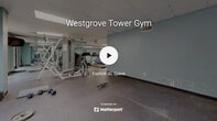 The gym at 4700 Westgrove Street in Raleigh, North Carolina, is a single-floor fitness facility designed to accommodate a range of workout needs. The space features a practical, open layout with distinct zones for cardio training, strength work, and functional exercise. Walls painted in a calming light blue set a clean, motivating tone throughout, while large floor-to-ceiling mirrors along one side visually expand the space and allow users to monitor their form during workouts.

The cardio area is equipped with a stationary recumbent bike and treadmills, positioned to take advantage of natural light from windows offering outdoor views. A stability ball and exercise mat provide a dedicated space for stretching and functional training. The strength training zone features a multi-station cable and weight machine, a weight bench, and an assortment of dumbbells, catering to both beginner and experienced lifters.

Flooring transitions between carpeted and hard rubber-tiled surfaces, strategically zoning the space for different activity types. The drop ceiling with recessed panel lighting ensures consistent, even illumination throughout. A wall-mounted television is also present, adding convenience for users during extended workout sessions. Overall, the facility offers a functional and accessible environment well-suited for everyday fitness use.