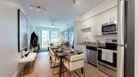 This thoughtfully designed single-floor residence combines modern aesthetics with functional living. The open-concept layout connects the kitchen, dining, and living areas seamlessly, creating a bright and airy atmosphere enhanced by large floor-to-ceiling windows that invite abundant natural light and offer views of the surrounding community.

The kitchen is outfitted with stainless steel appliances, including a range, microwave, and refrigerator, complemented by crisp white cabinetry, subway tile backsplash, and stone countertops. Wood-look tile flooring flows throughout the main living areas, adding warmth and continuity.

The living room features a distinctive accent wall in cool grey, a stylish gallery art arrangement, and sliding glass doors that open to a private balcony overlooking an outdoor pool area. The space is well-suited for both relaxing and entertaining.

The bedroom is a serene retreat highlighted by a striking abstract watercolor mural accent wall, wood-look flooring, and a walk-in closet with built-in shelving. The en-suite bathroom features an elongated vanity with a stone-tone countertop, undermount sink, and ample storage, providing a clean and polished finish. Track lighting and ceiling fans are featured throughout, adding both practicality and a contemporary touch to this well-appointed residence.
