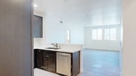 This contemporary apartment in Los Angeles offers 1090 square feet of thoughtfully designed living space. The unit boasts two bedrooms, including a generous primary bedroom measuring 220 square feet, and two full bathrooms. The open-concept layout seamlessly integrates the kitchen and living areas, creating an ideal space for both relaxation and entertainment.

The apartment features sleek, modern finishes throughout. Light-toned wood-look flooring runs through the main living areas and bedrooms, complementing the crisp white walls and creating a bright, airy atmosphere. Large windows in the bedrooms and living area flood the space with natural light and offer views of the surrounding area, including glimpses of palm trees that hint at the property's Southern California location.

The kitchen is a highlight, showcasing dark wood cabinetry contrasted with stainless steel appliances and light-colored countertops. A subtle backsplash adds texture, while the U-shaped layout maximizes functionality. The bathrooms continue the modern aesthetic with glass-enclosed showers, neutral-toned tile flooring, and contemporary fixtures.

Recessed lighting throughout the apartment provides adjustable ambiance, while a balcony off the living area offers outdoor space for enjoying the Los Angeles climate. The property's single-floor layout enhances accessibility and flow between rooms, making it an ideal urban dwelling for those seeking a blend of style and comfort in the heart of Los Angeles.