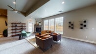 Located at 1881 Wiltsey Rd SE in Salem, Oregon, this single-story community clubhouse offers a well-appointed gathering space designed for comfort and functionality. The interior features a neutral color palette of warm grays and taupes, complemented by plush carpeting and wood-look flooring throughout.

The main lounge area is a standout feature, anchored by a stacked-stone corner fireplace and oversized windows that invite natural light and outdoor views. Leather seating in warm cognac and brown tones is arranged around a solid wood coffee table, creating an inviting and social atmosphere. Adjacent seating areas provide additional gathering space, including a cozy television lounge with a wall-mounted flat-screen, decorative wood-block wall art, and a coordinating media console.

Open shelving with wood and metal framework adds a modern-industrial touch throughout the communal areas. The fully equipped kitchen features white shaker cabinetry with matte black hardware, quartz countertops, subway tile backsplash, a stainless steel range hood, and hardwood-style flooring. A snack and refreshment area with built-in cabinetry offers added convenience.

The dedicated fitness room includes cardio equipment, a full dumbbell rack, medicine balls, and a ceiling fan, keeping the space comfortable during workouts. Recessed lighting and vaulted ceiling details throughout contribute to the open, airy ambiance of the clubhouse.