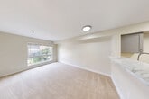 Located at 123 NE 112th Ave in Bellevue, WA, this 2-bedroom, 1-bathroom unit offers a thoughtfully designed layout across a single floor. The interior is finished with a clean, neutral palette of warm whites and beige tones throughout, creating a bright and welcoming ambiance.

The kitchen is a standout feature, outfitted with gray shaker-style cabinetry, marble-look countertops, a stainless steel sink with a modern gooseneck faucet, and stainless steel appliances including a refrigerator and range. Light wood-look flooring runs through the kitchen and hallway, adding warmth and continuity.

The open living area is carpeted and bathed in natural light from a large picture window overlooking lush greenery, providing a serene outdoor view. The space flows seamlessly from the kitchen via a peninsula counter.

Both bedrooms are carpeted and well-sized, with the primary bedroom featuring a large window with garden views. The second bedroom includes a built-in sliding closet. A utility area conveniently houses a stacked washer and dryer unit adjacent to the bathroom, which features a vanity with marble-look countertop and a framed mirror. A circular overhead light fixture in the hallway adds a subtle architectural touch throughout this well-maintained Bellevue residence.