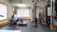 Located at 7800 Sporting Ln in Mechanicsville, Virginia, this single-floor fitness center is a well-equipped exercise facility designed to support a full range of workout routines. The space features durable rubber flooring throughout, providing a safe and supportive surface for all types of physical activity.

The cardio area is outfitted with multiple treadmills, a recumbent stationary bike, and elliptical trainers, each positioned near wood-trimmed windows fitted with adjustable blinds that allow natural light to fill the room. Wall-mounted flat-screen televisions are positioned for visibility from the cardio equipment, enhancing the workout experience.

A dedicated strength training section houses a multi-function cable machine equipped with a variety of attachments and an illustrated exercise reference guide, enabling users to perform a wide range of resistance exercises. A large wall-to-wall mirror with a wooden ballet barre runs along one side of the room, adding both functionality and a sense of spaciousness to the interior.

The facility also includes a water cooler with refill jugs for convenient hydration. Neutral gray walls, warm wood accents on the baseboards and window trim, and flush-mounted lighting contribute to a clean, functional aesthetic. The layout is organized to maximize usable floor space while keeping equipment easily accessible.