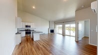 Located in Suamico, Wisconsin, this thoughtfully designed one-bedroom, one-bathroom home offers a modern aesthetic with high-quality finishes across a well-utilized single floor. The open-concept kitchen and living area is the heart of the home, showcasing soaring vaulted ceilings that amplify the sense of space. The kitchen is outfitted with crisp white shaker cabinetry extending nearly to the ceiling, dark granite countertops, a central island with a sink, and a full suite of stainless steel appliances. Warm hardwood-style flooring flows seamlessly throughout the entire home. The living area features a clean-lined corner fireplace and large sliding glass doors that flood the space with natural light and frame peaceful outdoor and waterfront views. The bedroom is a comfortable retreat with its own sliding glass door to the outside, a wall-mounted climate control unit, and generous natural light. The bathroom is finished with white shaker vanity cabinetry, dark granite counters, and a pendant light fixture. A dedicated laundry room houses a full-size front-loading washer and dryer alongside wire shelving for added storage. This home combines modern design with practical functionality in a serene Wisconsin setting.