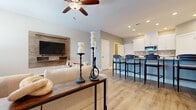 This two-story home offers a thoughtfully designed layout spread across two floors, with the main living areas on the ground level and the bedrooms above. The open-concept main floor seamlessly connects the living room and kitchen, creating an inviting, social atmosphere. The living room features light hardwood flooring, a ceiling fan, large windows that allow natural light to pour in, and a wood-accented media wall. The kitchen is equipped with white shaker cabinetry, stainless steel appliances including a gas range and French door refrigerator, white countertops, and a breakfast bar with stylish navy blue seating. Upstairs, the spacious primary bedroom features plush carpeting, a ceiling fan, and a connected en-suite bathroom with white cabinetry and a large vanity mirror. The two additional bedrooms are well-sized with carpet flooring and bright windows. Three full bathrooms serve the home, each finished with white cabinetry, wood-look flooring, and clean, modern fixtures. A dedicated laundry room houses a full-size washer and dryer. Throughout the home, a neutral warm-gray color palette and consistent wood-look flooring create a cohesive, modern aesthetic that is both comfortable and functional.