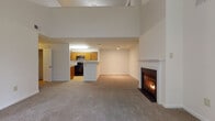Located at 9901 Gable Ridge Terrace in Rockville, MD, this two-floor residence offers a thoughtfully designed layout with bright, open living spaces. The main level centers around a generous living area highlighted by soaring two-story ceilings and a classic wood-burning fireplace with a white-trimmed mantle, creating a warm and inviting focal point. Plush wall-to-wall carpeting flows throughout the main living area, while the adjacent kitchen features warm oak cabinetry, light countertops, and black appliances including a gas range. A pass-through counter connects the kitchen to the living space, enhancing the open feel. The lower-level bathroom includes hardwood-style flooring, a tub-shower combination with tile surround, wood-toned vanity, and a conveniently tucked-in stacked washer and dryer unit. Upstairs, the bedrooms are carpeted and well-lit by natural light streaming through large windows that frame views of surrounding greenery. One bedroom opens directly onto an outdoor balcony, while another features a vaulted ceiling with a ceiling fan and a spacious built-in closet with shelving. A second full bathroom mirrors the clean, functional design of the first. Throughout the home, neutral tones and abundant natural light create a calm, comfortable ambiance.
