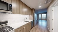 This 420 square foot apartment, located at 1940 Webster St in Oakland, CA, offers a thoughtfully designed living space on a single floor. The open-plan layout maximizes the available area, creating a sense of spaciousness despite its compact size. The living room is adorned with wide-plank, wood-look flooring that extends throughout the apartment, lending warmth and continuity to the space. Large windows and a glass door leading to a balcony flood the area with natural light, enhancing the room's airy feel.

The kitchen is a highlight, featuring sleek, light wood cabinetry that extends to the ceiling, maximizing storage. Modern stainless steel appliances, including a built-in microwave and range, complement the clean lines of the white quartz countertops and backsplash. A undermount sink with a contemporary faucet completes the kitchen's efficient design.

The bathroom, while compact, is well-appointed with a full-sized bathtub and shower combination, enclosed by a curved shower rod for added space. The same wood-look flooring continues into this space, creating a cohesive look throughout the apartment. Recessed lighting in all areas provides even illumination, with an additional track lighting fixture in one section for task or accent lighting as needed.

Overall, this apartment offers a contemporary, low-maintenance living solution, ideal for those seeking a modern urban lifestyle in the heart of Oakland.
