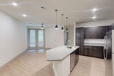 Located at 6131 Louetta Road in Spring, TX, this thoughtfully designed one-bedroom, one-bathroom residence offers a clean, modern aesthetic with quality finishes throughout. The open-concept kitchen and living area serves as the heart of the home, anchored by a central kitchen island with a granite countertop, undermount sink, and stylish pendant lighting. Rich, dark-toned shaker-style cabinetry lines the kitchen walls, complemented by white tile backsplash, granite counters, and a full suite of stainless steel appliances including a refrigerator, range, and microwave. Light wood-look flooring flows throughout the main living area, which benefits from natural light through sliding glass doors and a ceiling fan overhead. The bedroom offers plush carpeting, a ceiling fan, and a window with blinds, creating a comfortable and restful retreat. A dedicated closet provides ample storage. The bathroom is well-appointed with dark cabinetry, granite countertops, a single undermount sink, a tub-shower combo with white subway tile surround, and light wood-look flooring. Recessed lighting and clean white walls give the entire unit a bright, welcoming ambiance.
