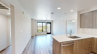 Located at 525 N 7th St in San Jose, California, this modern 2-bedroom, 2-bathroom residence offers a thoughtfully designed single-floor layout with contemporary finishes throughout. The open-concept kitchen and living area serves as the heart of the home, featuring light wood-tone cabinetry, white quartz countertops, stainless steel appliances including a French door refrigerator, range, microwave, and dishwasher, all set atop light hardwood-style flooring. Large black-framed windows and a glass balcony door in the living area flood the space with natural light while offering open views of the surrounding San Jose cityscape and palm trees. The spacious primary bedroom includes plush carpeting, a generous walk-in closet, and an additional closet, connected to a hallway leading to the rest of the unit. The second bedroom, also carpeted, features a window with natural light. Both bathrooms are finished in a clean, minimalist style with light wood vanities, white quartz surfaces, and light hardwood-style flooring; one bathroom includes a soaking tub. Two closets provide ample storage throughout. The overall aesthetic is clean, bright, and modern, with a neutral palette that lends itself to a variety of interior styles.