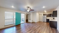This single-story unit is designed with a clean, modern aesthetic throughout. The open-concept kitchen and living area serves as the heart of the space, where rich, dark-stained wood cabinetry is paired with light countertops and a full suite of stainless steel appliances, including a refrigerator, dishwasher, and range. A stacked washer and dryer unit is conveniently tucked into a dedicated nook adjacent to the kitchen. Recessed lighting illuminates the space, which flows seamlessly across warm wood-style flooring that extends throughout the unit.

The living area is generously proportioned, featuring a ceiling fan with integrated lighting and access to a private balcony through a striking teal door. From the balcony, views of the surrounding courtyard and building exterior are framed by metal mesh railings, offering a modern outdoor retreat.

The bedrooms are well-sized, each featuring ceiling fans, recessed lighting, and the same consistent wood-style flooring. The bathroom is finished with dark vanity cabinetry, white countertops, chrome fixtures, and a full tub-shower combination surrounded by large-format neutral tile, creating a cohesive and polished look.