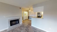 This single-floor residence offers an open and functional layout that seamlessly connects the main living spaces. The living room serves as the heart of the home, highlighted by a tiled fireplace with a classic white mantle that adds warmth and character to the space. Wood-look flooring flows throughout, complementing the neutral gray wall tones and creating a cohesive, modern aesthetic. A ceiling fan with integrated lighting adds both style and practicality overhead, while a textured ceiling adds subtle dimension.

The kitchen is designed for convenience and accessibility, featuring a pass-through counter that opens directly to the living area. It is equipped with stainless steel appliances, including a microwave and range, set against light cabinetry and a clean countertop surface — providing ample workspace for cooking and entertaining.

Visible from the main living area, a dedicated in-unit laundry space is neatly tucked into its own alcove, offering the added convenience of a washer and dryer within the home.

Natural light filters through the space, enhancing the bright, airy feel cultivated by the light flooring and pale wall colors. The overall ambiance is clean, contemporary, and move-in ready, making it a practical and comfortable living environment.