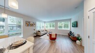 This thoughtfully designed single-floor residence offers 3 bedrooms, 2 bathrooms, and a closet, all connected by a clean, light-filled hallway with light wood-tone flooring that runs throughout the home. The open-concept kitchen and living area serves as the heart of the space, where the kitchen features light wood cabinetry, stainless steel appliances, a white quartz countertop island, subway tile backsplash, and pendant lighting. An adjacent dining area with window access makes the space feel airy and functional. The living room is generously proportioned and framed by large windows on multiple walls that invite sweeping views of mature trees, filling the room with natural light and a sense of connection to the outdoors. The primary bedroom is a comfortable retreat, benefiting from its own access to a well-appointed en-suite bathroom complete with a modern floating vanity, clean white countertops, and a glass-enclosed shower. A second full bathroom, equally refined in its finishes, serves the remaining bedrooms. Each bedroom features large windows with lush exterior views, light-toned flooring, and neutral wall colors that create a calm, inviting atmosphere. The overall design is modern and cohesive, with a bright, neutral palette throughout.
