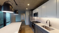 Located in Chicago's vibrant River North neighborhood, this single-floor unit at 608 N Wells St showcases a compelling blend of industrial and contemporary design. Exposed concrete ceilings run throughout the space, providing a raw architectural contrast against the refined, modern finishes below.

The living area is anchored by expansive floor-to-ceiling windows framed in dark metal, offering sweeping views of the Chicago skyline. A prominent concrete column adds to the industrial character while reinforcing the structural aesthetic. Wood-look plank flooring flows consistently throughout the unit, warming the otherwise industrial palette.

The kitchen is thoughtfully designed with gray lower cabinetry accented by brushed gold hardware, white upper cabinets, and a herringbone-patterned tile backsplash. Stainless steel appliances, quartz countertops, and a matte black faucet complete the space. A large island provides additional workspace and a pendant light adds a stylish focal point.

Two bathrooms echo the unit's design language. One features a glass-enclosed walk-in shower with white subway tile and matte black fixtures, while the second includes a full soaking tub. Both feature gray vanities with quartz countertops and backlit mirrors. An in-unit stacked washer and dryer adds practical convenience.